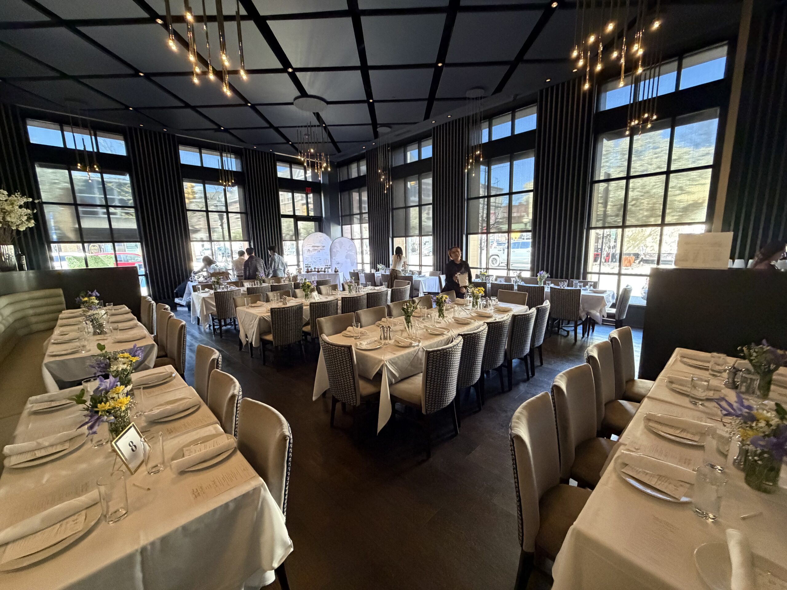 The Vine & Oak Tavern private-event room in Cranford NJ, set for a party Vine & Oak Tavern private-event room set for a party — long white-clothed tables, floor-to-ceiling windows, and modern chandeliers in downtown Cranford, NJ