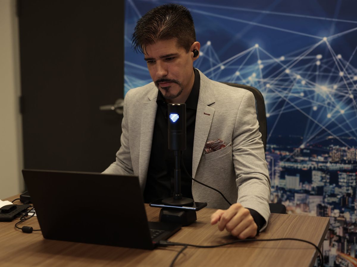 Man at a desk with a laptop, wearing an earpiece for a call
