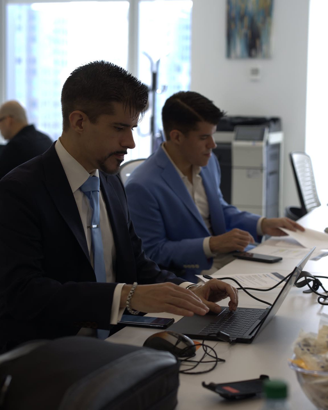 Two people working side by side at laptops on a long office desk